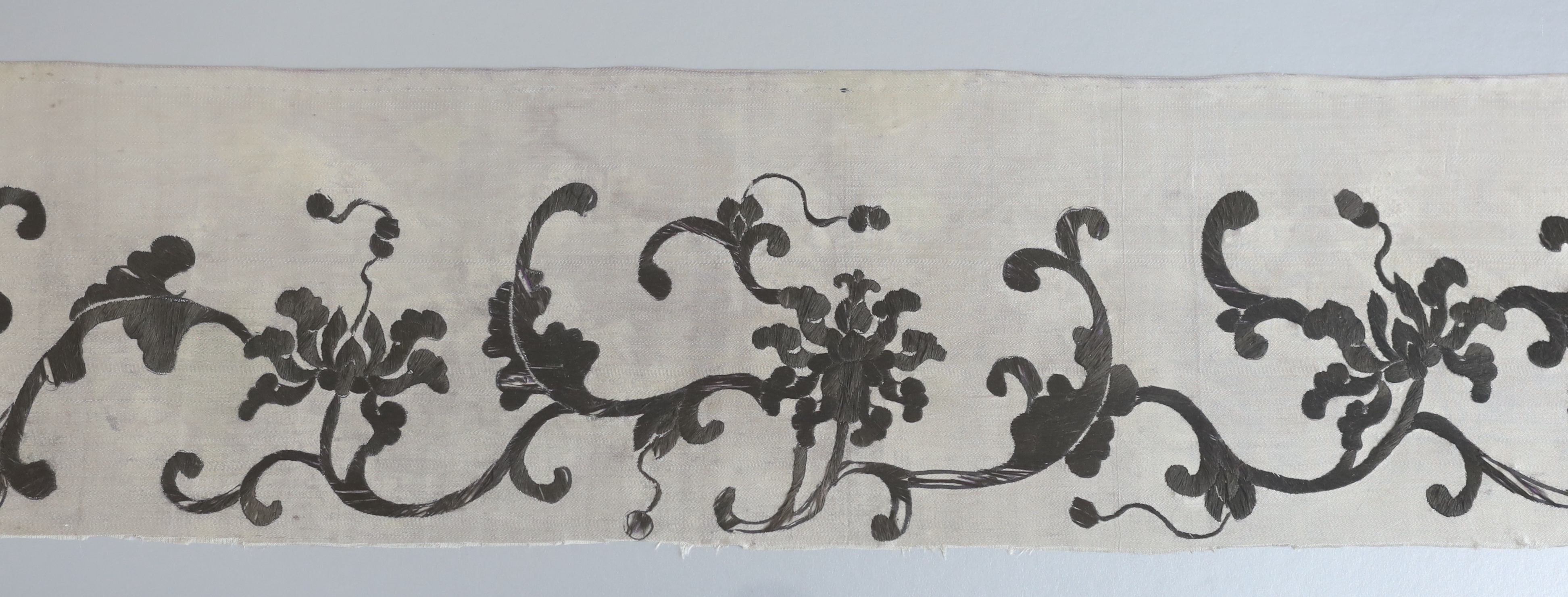 A late 19th century Chinese black and cream silk embroidery, mounted together with an inscribed calligraphic stone, a pair of white metal chop sticks and a similar dish, embroidery: 5.5cm wide, 105cm long
